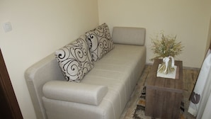 A living room with a sofa, patterned pillows, a small wooden side table with a vase of dried flowers, and a wooden floor. - Agrotourism Vinia (Bjelovar)