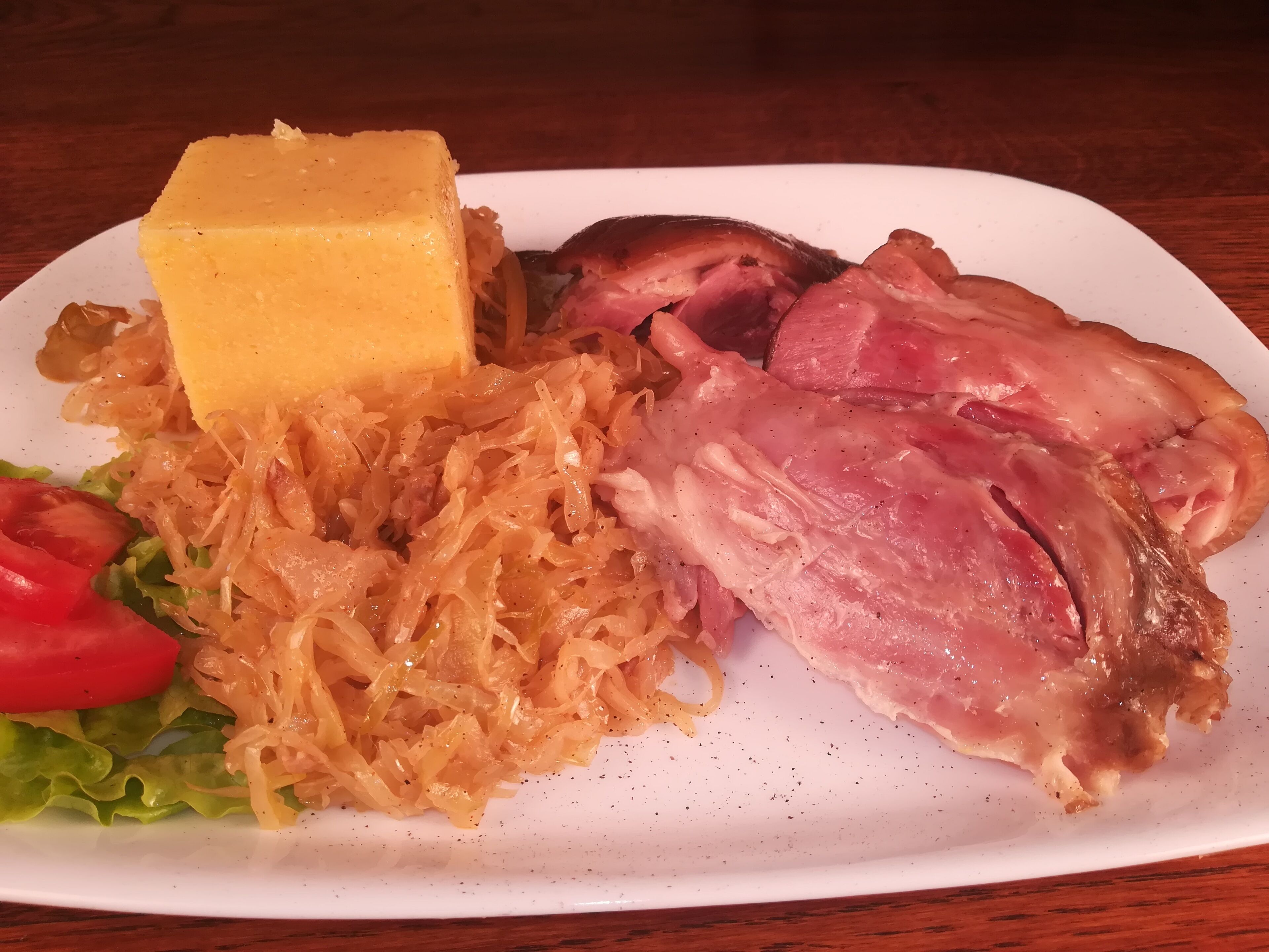 Un plato con una rebanada de queso, tocino, chucrut, lechuga y tomate.