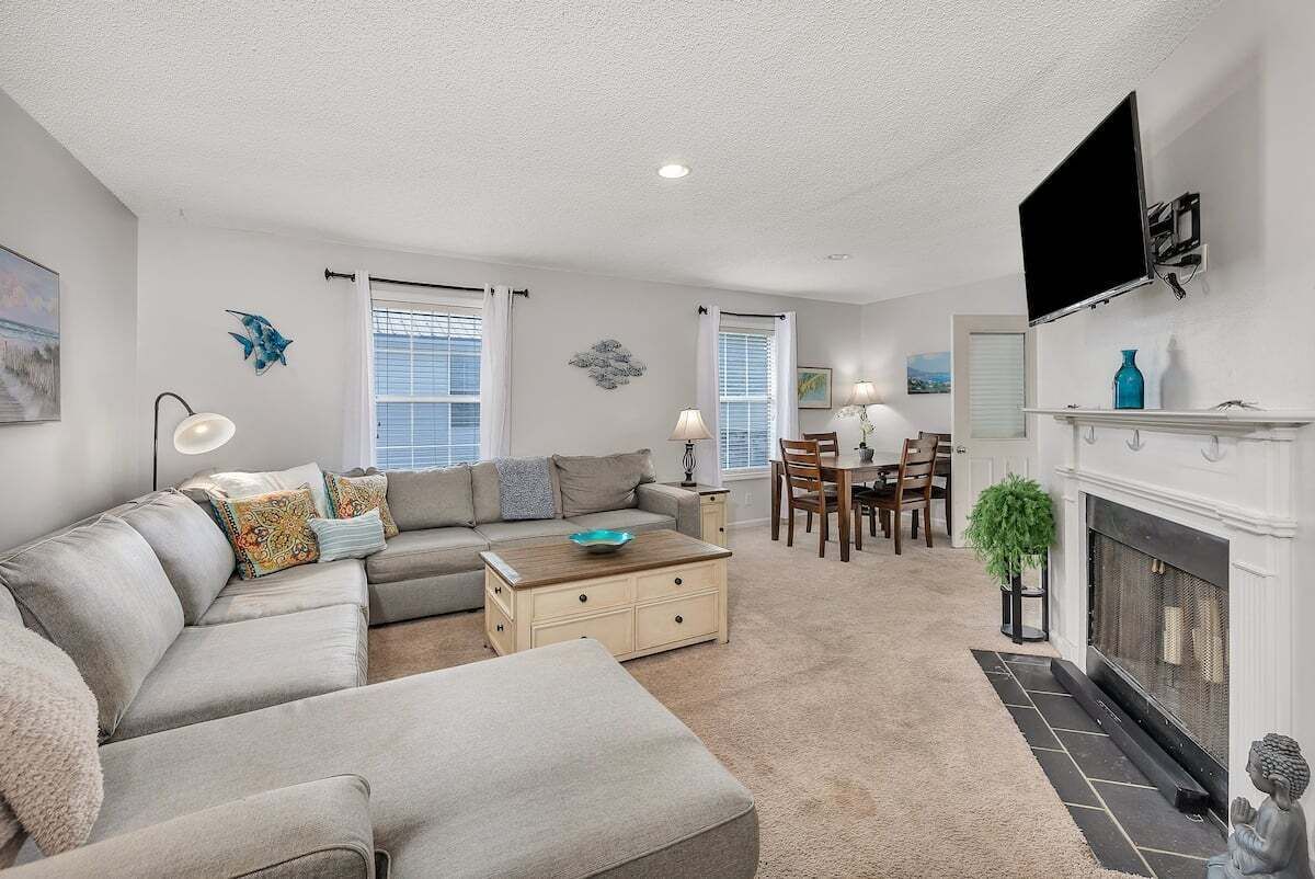 A living room with a sectional sofa, a coffee table, a fireplace, and a dining area with chairs and a table.