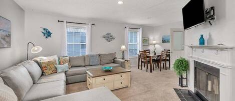 A living room with a sectional sofa, a coffee table, a fireplace, and a dining area with chairs and a table.