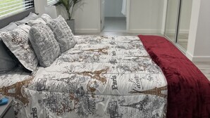 Une chambre à coucher avec un lit, une table de chevet, un plaid rouge, une plante en pot et une fenêtre avec des stores.