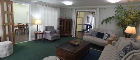 A living room with a green carpet, two sofas, a coffee table, a cabinet, and a dining area with a table and chairs.
