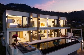 A modern multi-story house with a large glass pool, multiple bedrooms, and a dining area. - Luxury 5 Bedroom Modern Villa - KBR17 (Koh Samui)