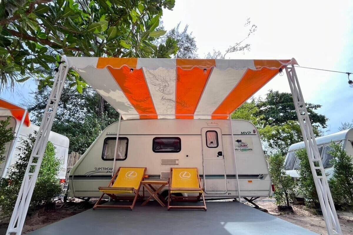 A campervan with a covered seating area and two lounge chairs.