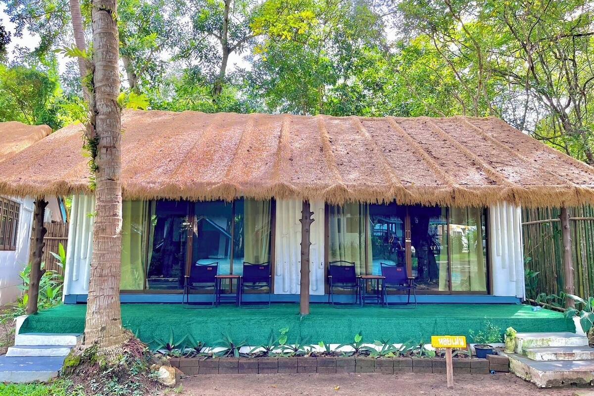 A thatched-roof structure with a covered seating area, surrounded by greenery.