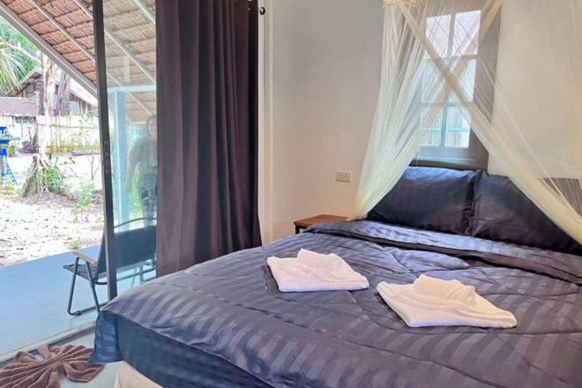 A bedroom with a bed, a window with curtains, and a view of the outside.