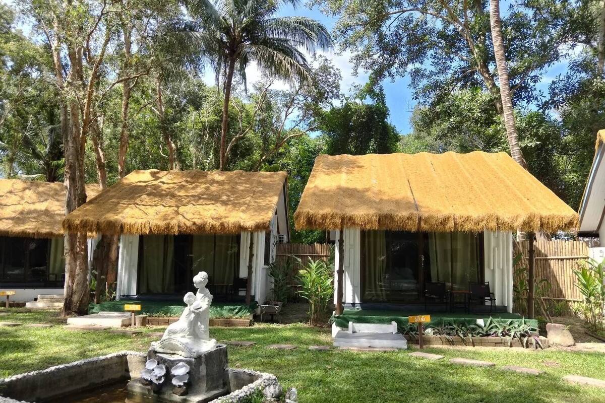 A tropical resort with thatched-roof huts, a statue, and a small water feature.