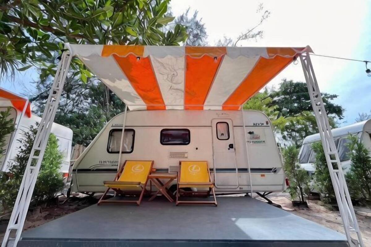 A recreational vehicle with a covered patio area, two lounge chairs, and a ladder.