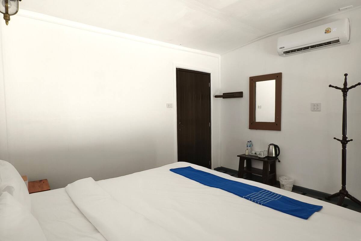 A hotel room with a bed, a nightstand, a mirror, an air conditioning unit, and a floor lamp.
