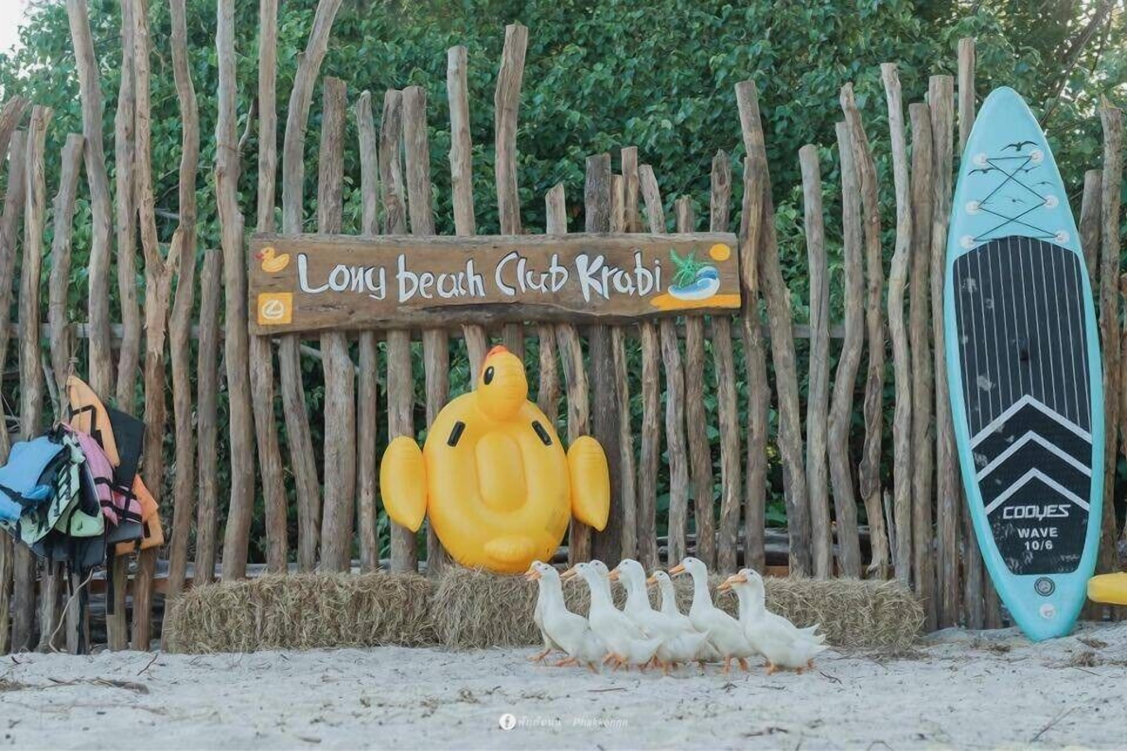 Ein Holzschild mit dem Schriftzug 'Long Beach Club Krabi' und einem großen, aufblasbaren Enten.