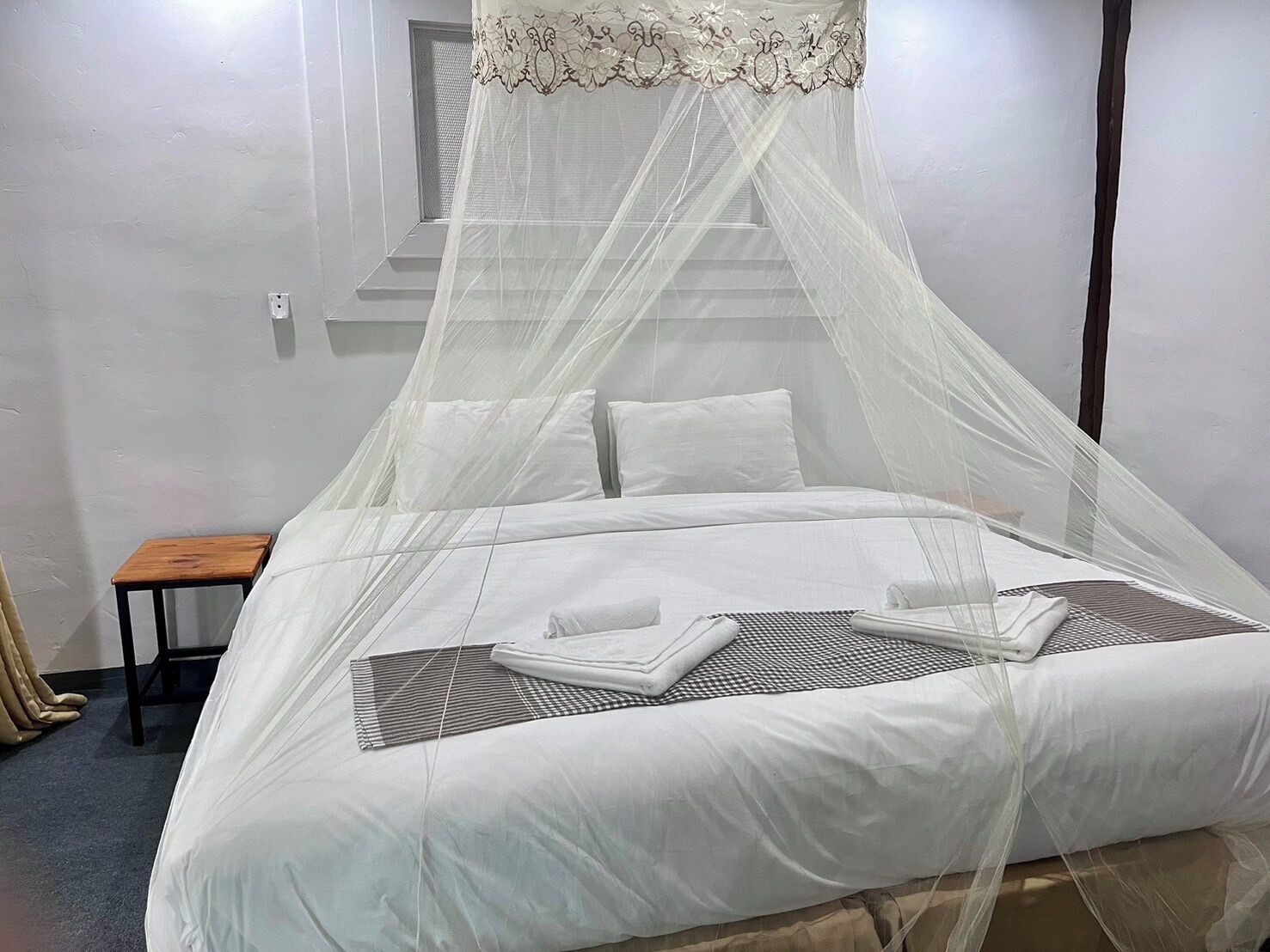 A neatly made bed with white linens, a canopy, and a small wooden nightstand beside it.