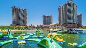 Une zone riveraine dotée de structures gonflables pour jeux aquatiques, d’un quai et, en arrière-plan, d’immeubles de grande hauteur.