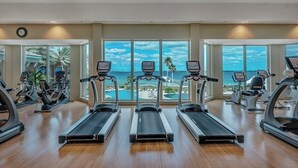 Une salle de sport équipée de tapis de course, de vélos d’appartement et d’appareils elliptiques, avec de grandes fenêtres offrant une vue sur l’océan.