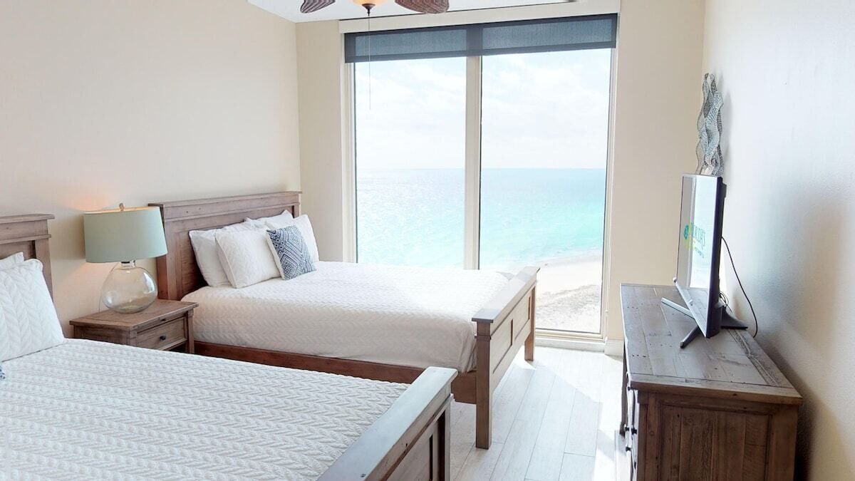 Habitación de hotel con dos camas, un televisor y un ventanal grande con vistas al mar.