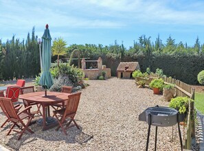 An outdoor patio with a round wooden table and chairs, a barbecue grill, and a small house-like structure.