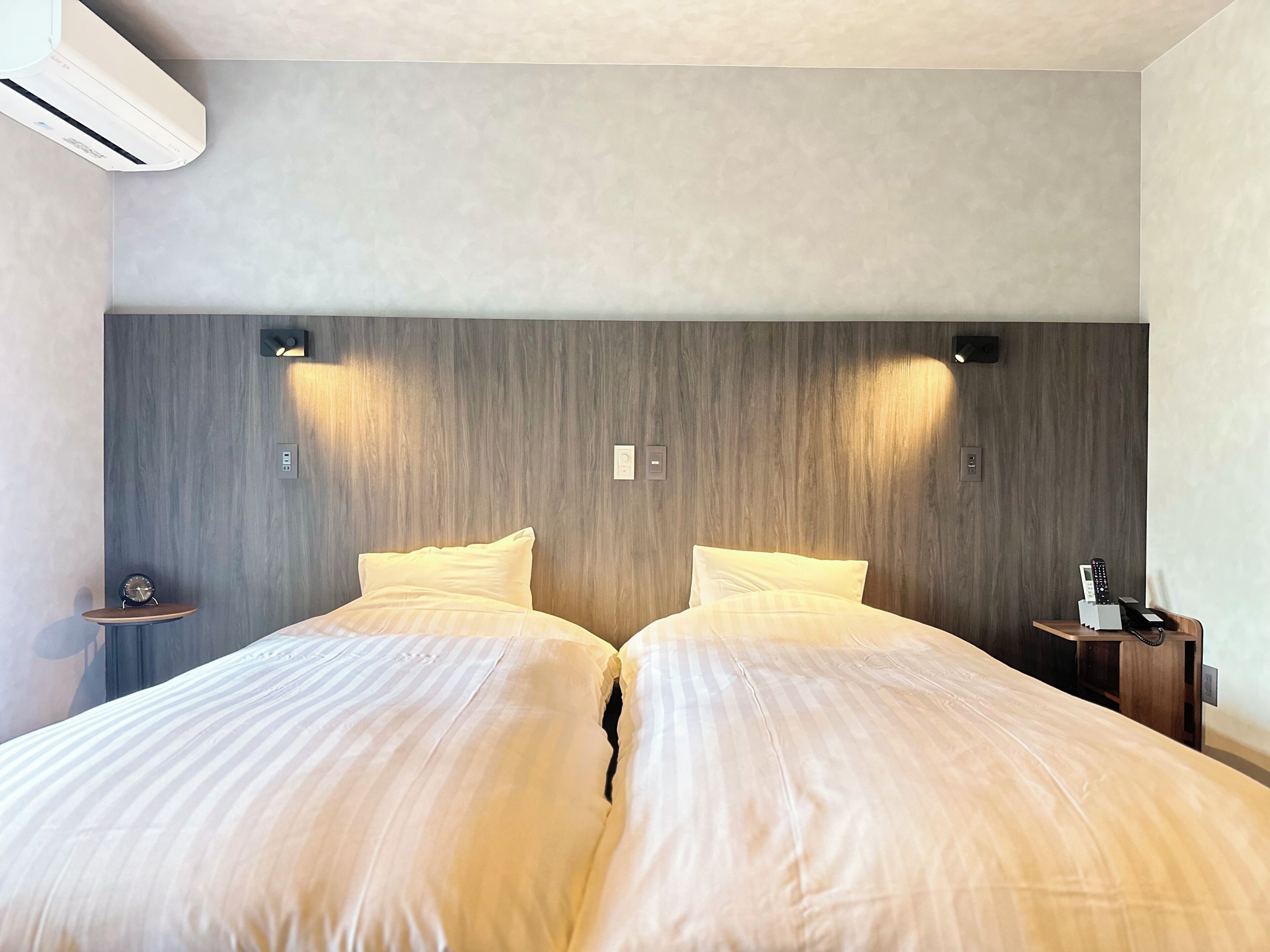 A double bed with two pillows, a bedside table with a lamp, and a wall-mounted air conditioner.