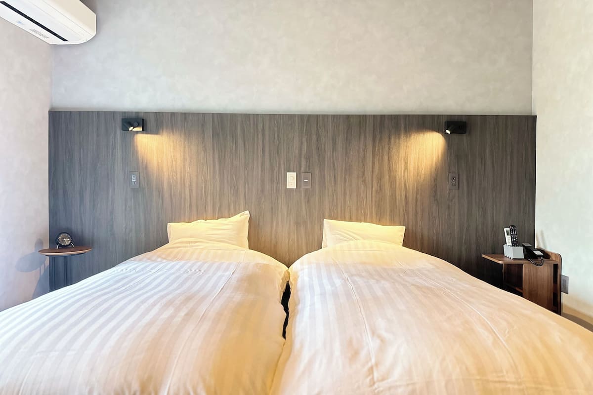 Un lit double avec deux oreillers, une table de chevet avec une lampe et un climatiseur fixé au mur.