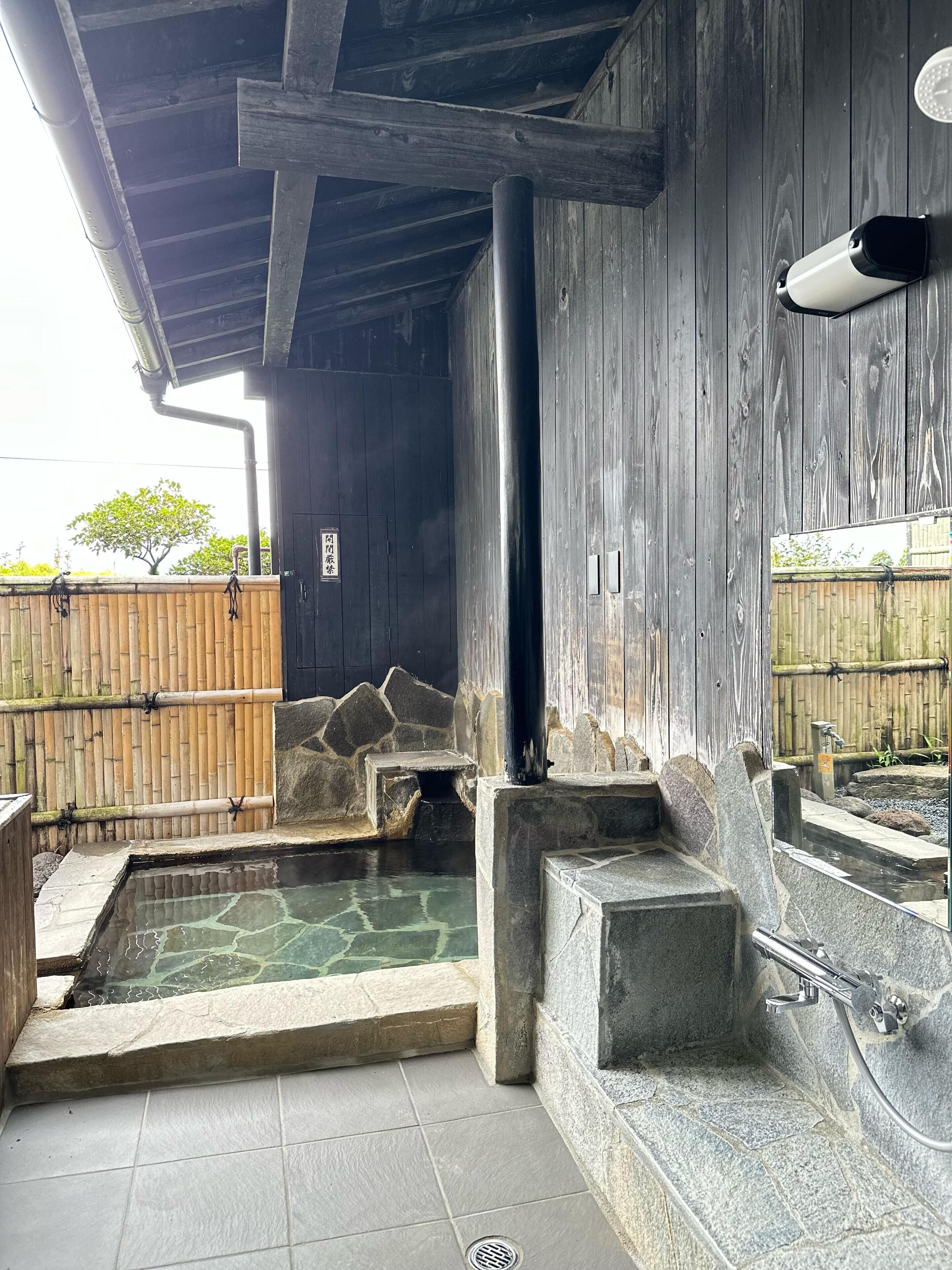 Ein traditionelles japanisches Onsen mit Steinbädern, Holzvertäfelung und einem Bambuszaun im Hintergrund.