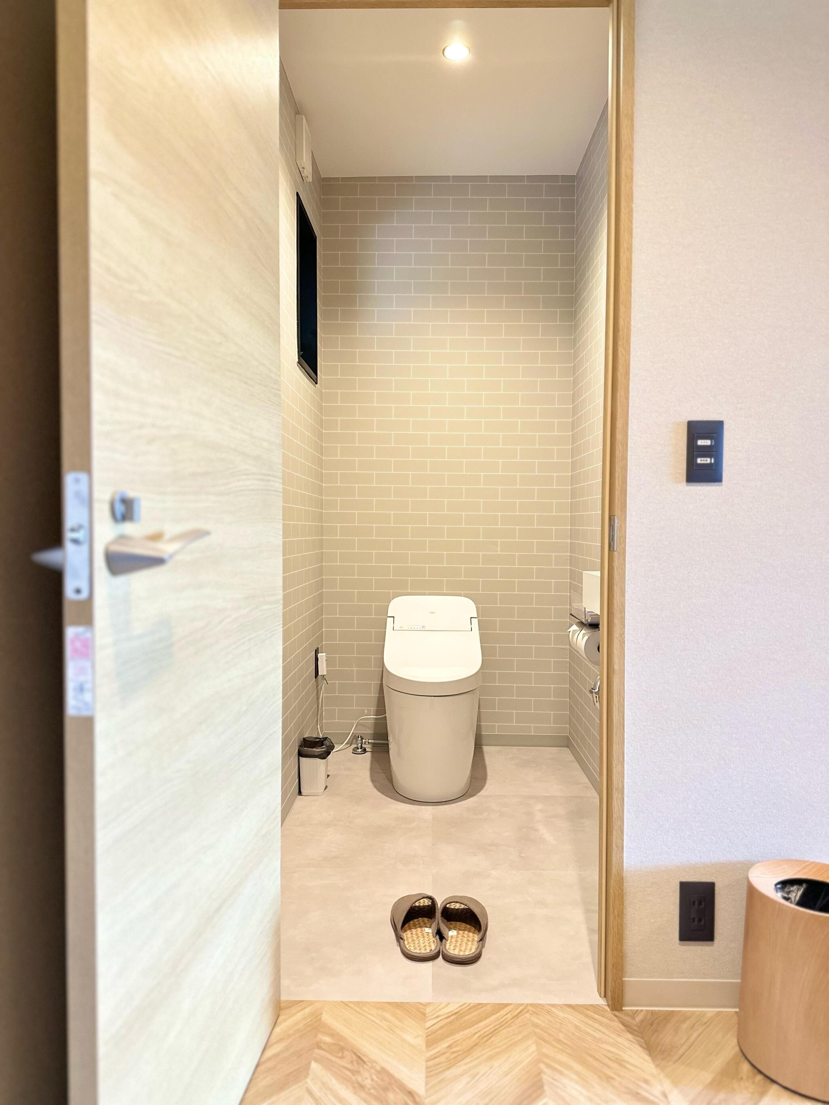 A compact bathroom with a toilet, a trash bin, and a pair of slippers on the floor.