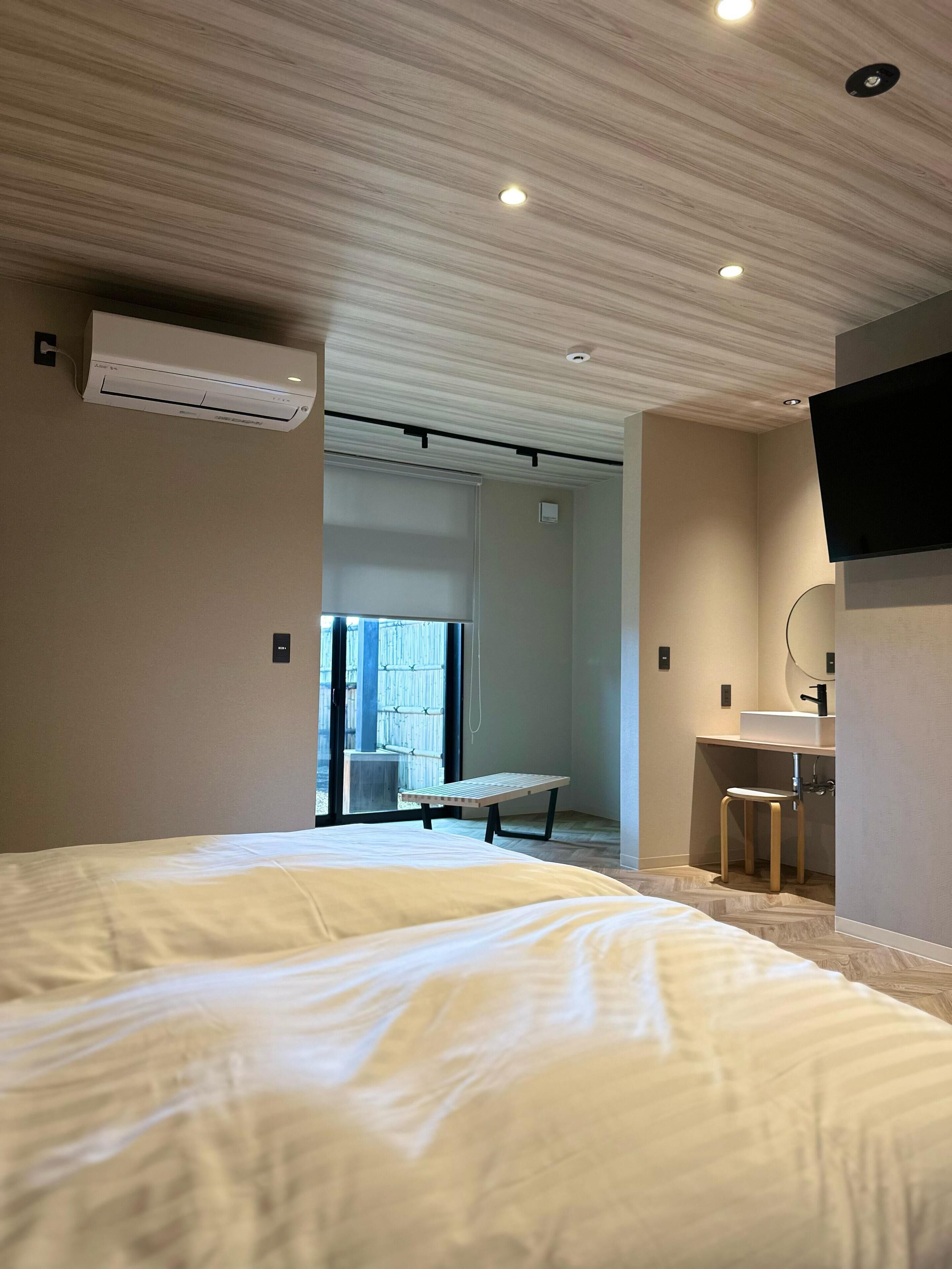 A hotel room with a large bed, a desk with a chair, a TV mounted on the wall, and an air conditioning unit on the ceiling.