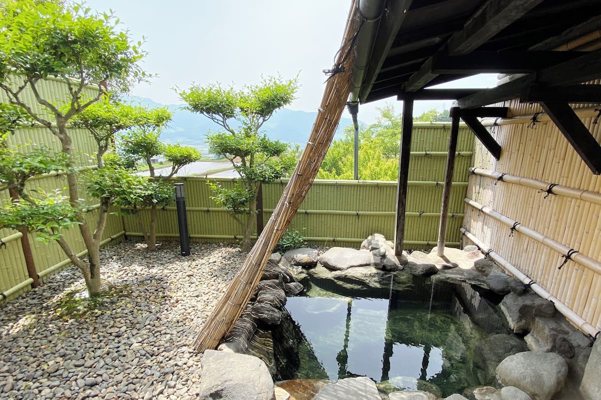 Un jardin japonais traditionnel avec un bassin à carpes koï, des clôtures en bambou et une structure en bois.