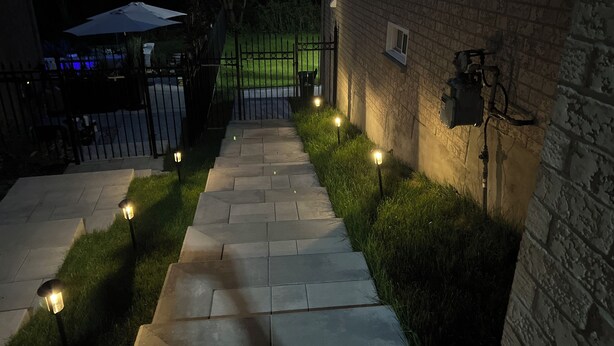 A stone pathway leading to a gated entrance, surrounded by grass and illuminated by ground lights. - Bright 2BR unit | Free Parking | Family Friendly | Richmond Hill (Richmond Hill)