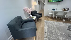 A modern living room with grey armchairs, a white coffee table, a TV mounted on the wall, and a dining area with a table and chairs. - Bright 2BR unit | Free Parking | Family Friendly | Richmond Hill (Richmond Hill)