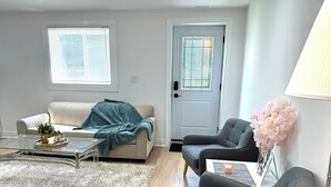 A living room with a beige sofa, a grey armchair, a glass coffee table, a white rug, and a door with a frosted glass window. - Bright 2BR unit | Free Parking | Family Friendly | Richmond Hill (Richmond Hill)
