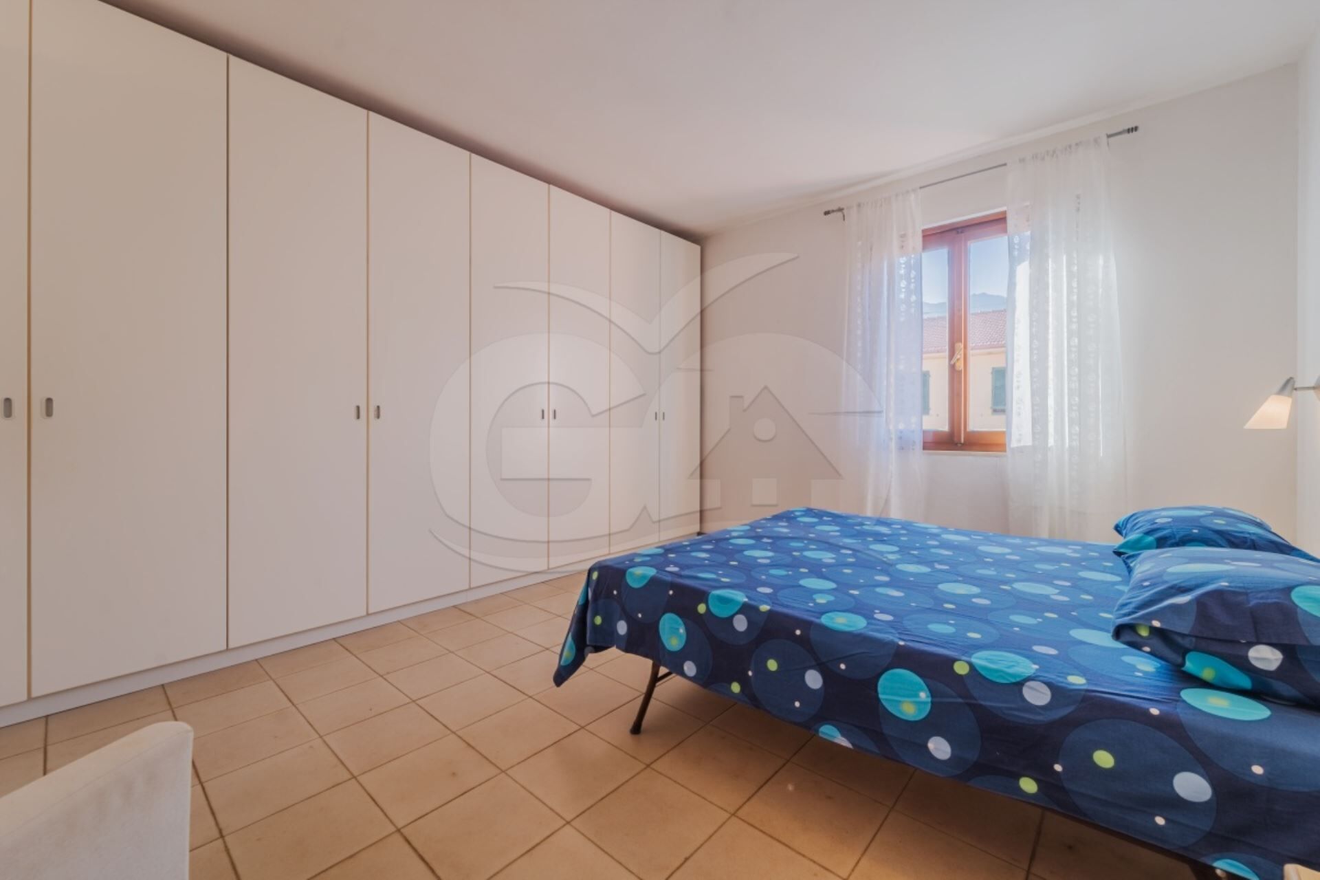 A bedroom with a bed, a wardrobe, and a window with curtains.