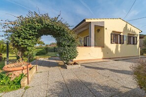 Une maison de plain-pied à l’extérieur jaune, dotée d’un petit porche et d’un jardin agrémenté d’un arbre et d’un bac à fleurs.