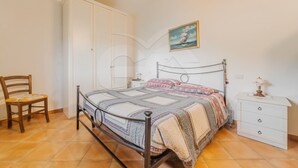Un dormitorio con cama, una silla, una mesita de noche, un aparador y un cuadro en la pared.