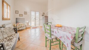 Un salón amplio con sofá, una mesa de comedor con sillas, televisor y una cocina visible a través de un vidrio.