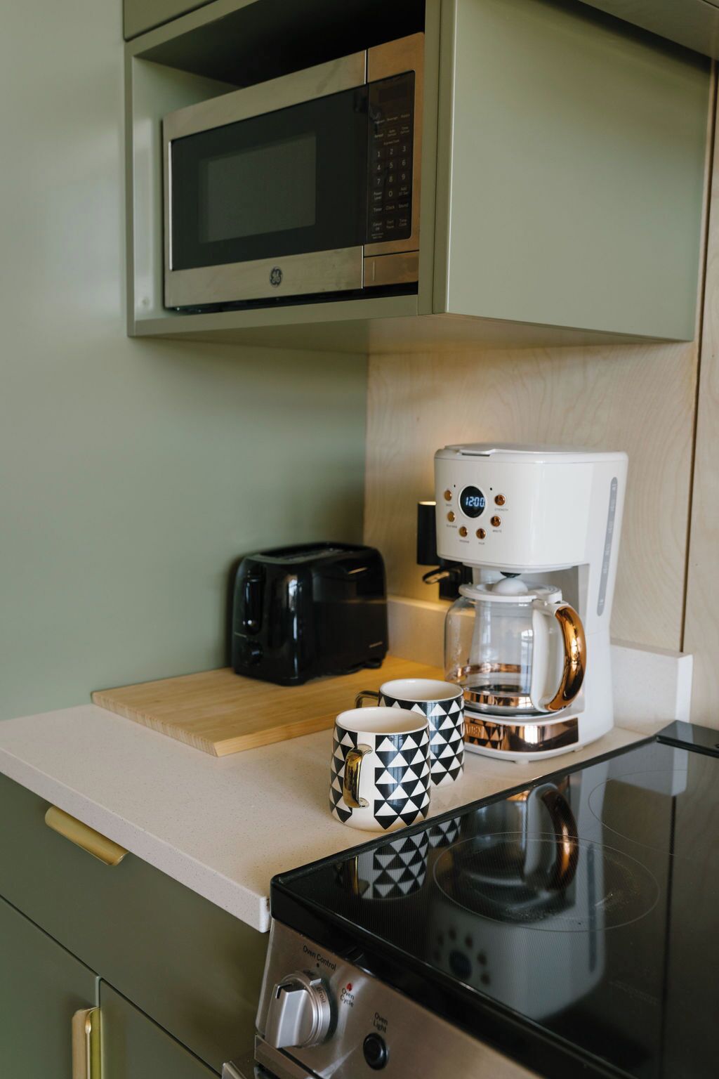 Een keuken met een magnetron, broodrooster, koffiezetapparaat en een fornuis.