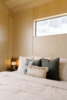 Un dormitorio con techo de madera, un ventanal grande y una cama con muchos almohadones.