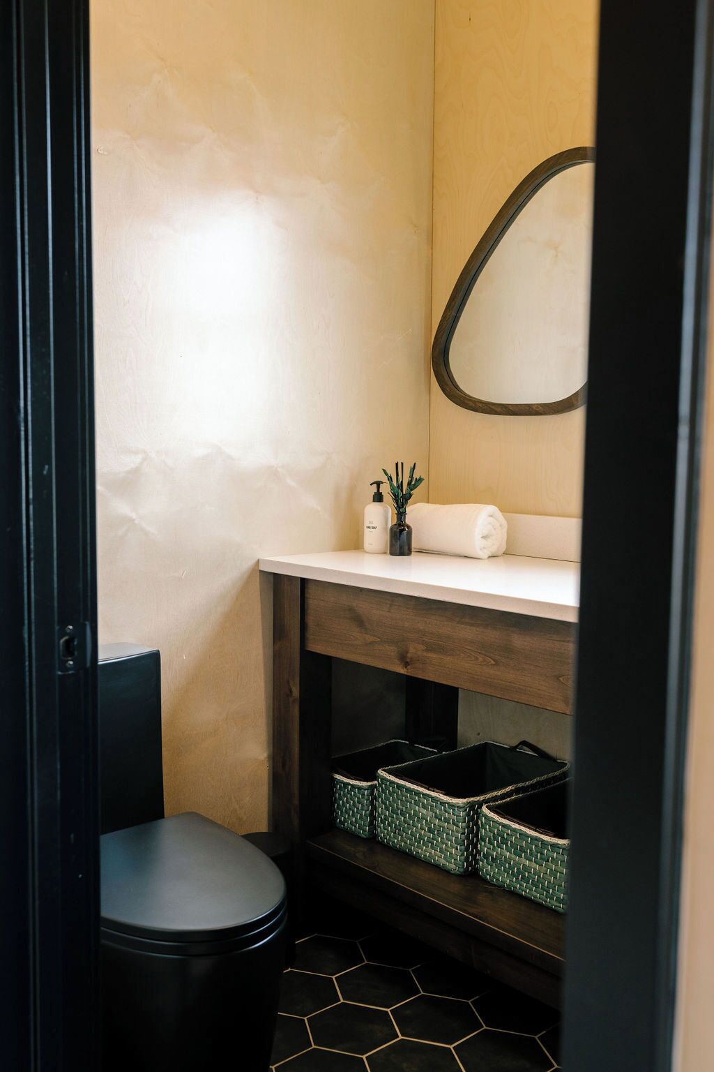 Une petite salle de bain comprenant des toilettes, un lavabo avec un miroir et une étagère avec des paniers.