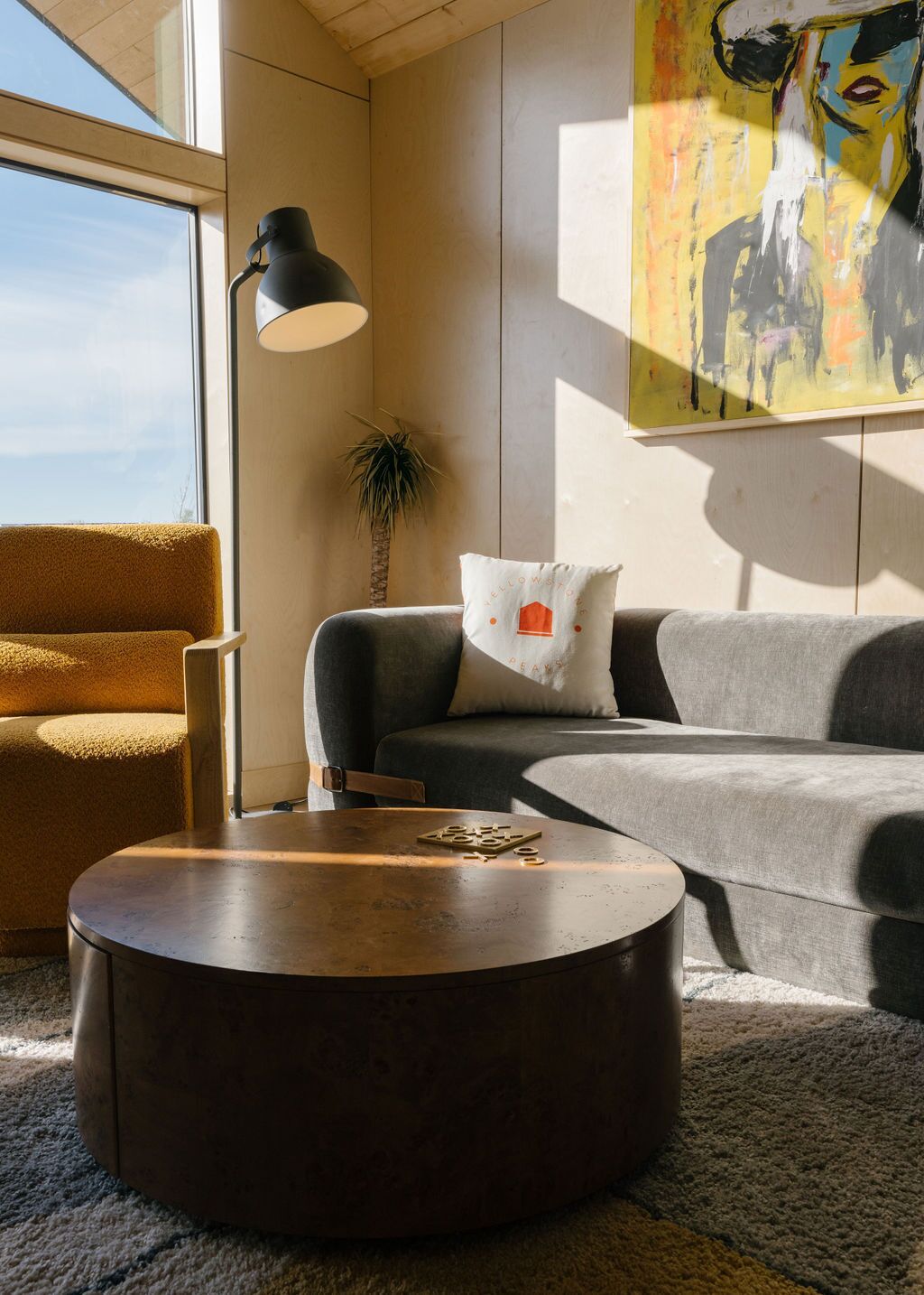 A modern living room with a round coffee table, a sofa, a chair, and a painting on the wall.