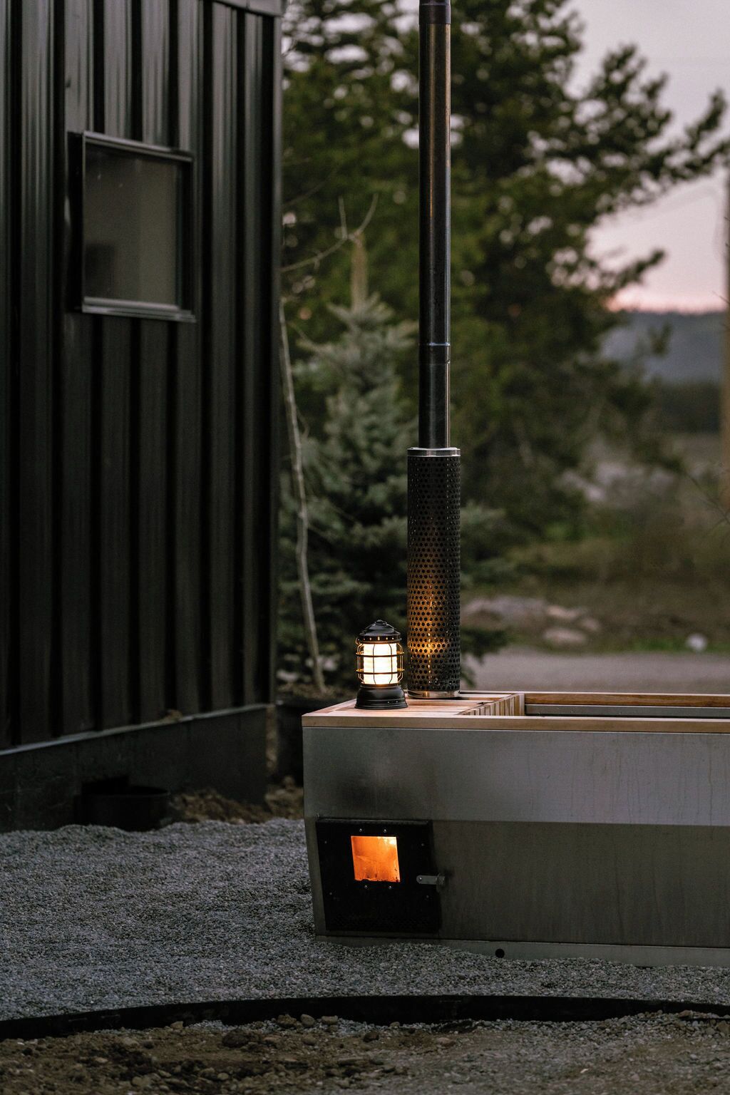 A metal structure with a vertical pole and a rectangular base, possibly a heater or outdoor equipment, next to a building with a window.