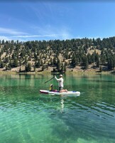 Una persona en una tabla de remo en un lago tranquilo con una ladera boscosa al fondo.