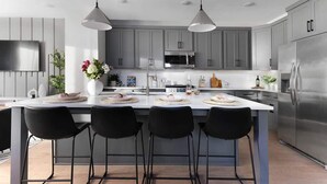 Une cuisine moderne avec des meubles gris, un réfrigérateur en acier inoxydable, un four à micro-ondes et un grand îlot central doté de tabourets de bar.