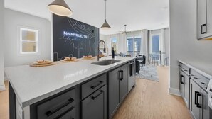 Une cuisine moderne dotée d’un grand îlot central, de meubles de couleur noire et d’un éclairage suspendu.