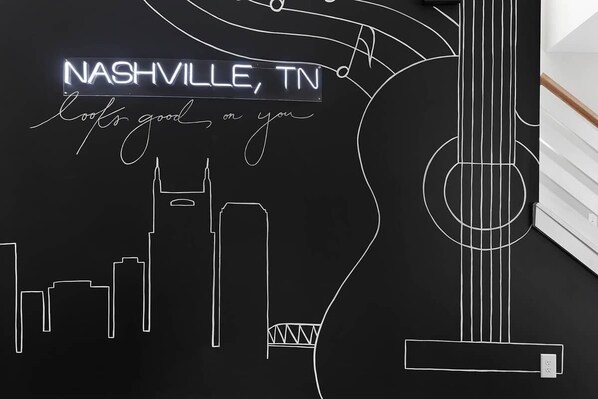 Una pizarra con contornos blancos de una guitarra y el horizonte de Nashville, con el texto 'Nashville, TN' y 'Te queda genial'.