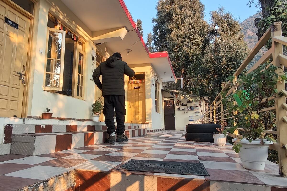 Una persona de pie frente a la entrada de un edificio con piso a cuadros, plantas en macetas y una escalera que sube.