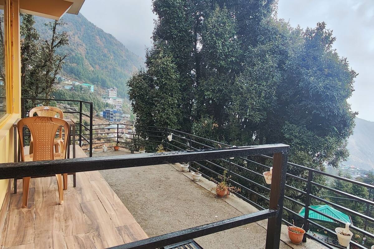 Una terraza de madera con baranda metálica, plantas en macetas y vistas a un paisaje montañoso.