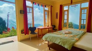 A bedroom with a bed, a desk, and two windows offering a view of the outdoors.