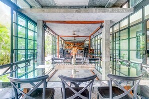 An indoor dining area with glass tables and chairs, a central decorative vase, and a ceiling fan.