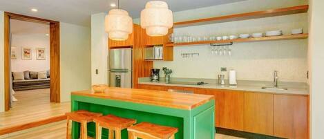 Une cuisine moderne avec un îlot central vert, des tabourets en bois et des luminaires suspendus.
