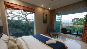Habitación de hotel con una cama grande, una silla y un balcón con vistas a árboles y montañas.