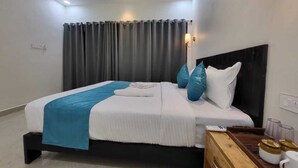 Une chambre d’hôtel moderne avec un lit bien fait, une table de chevet en bois sur laquelle se trouve une machine à café, et une grande fenêtre avec des rideaux.