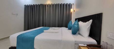 A modern hotel room with a neatly made bed, a wooden nightstand with a coffee maker, and a large window with curtains.