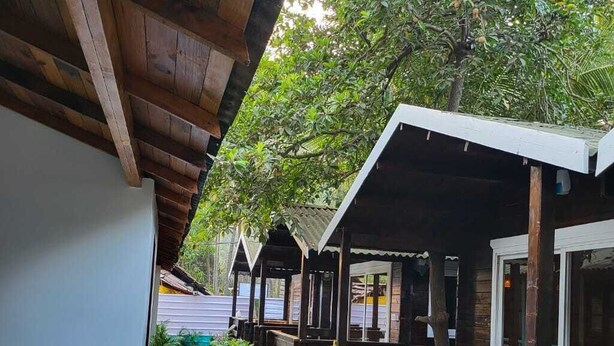 Un espace extérieur abrité, doté de bancs en bois et de plantes en pot, qui mène à un bâtiment aux grandes fenêtres.
